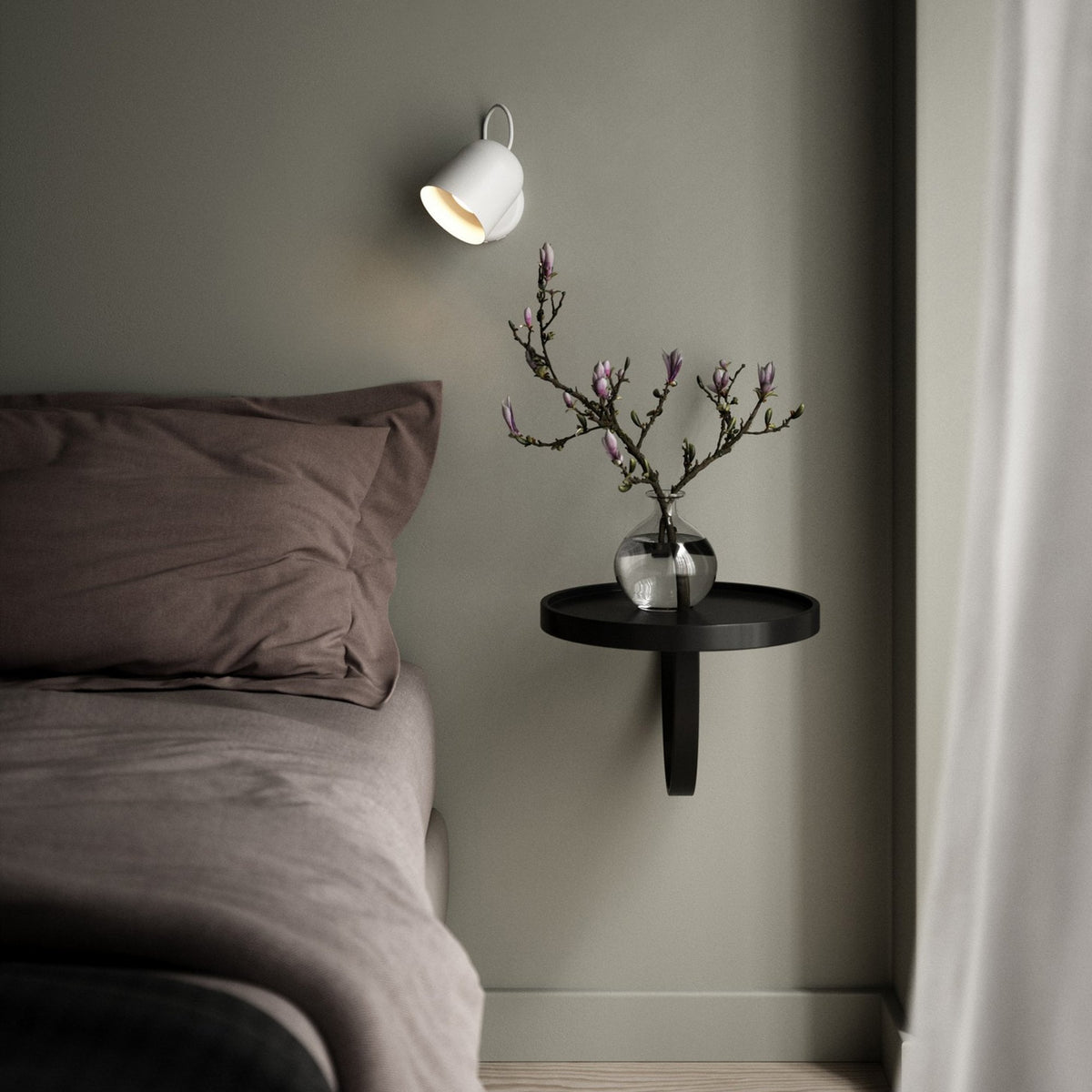 A white wall light illuminates a modern bedroom with a green wall and a minimalist bedside table.