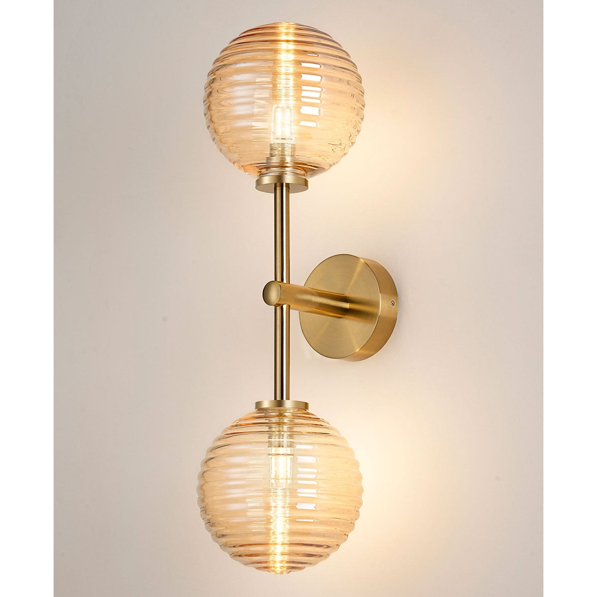 A brass wall light with two amber ribbed glass globe shades emitting a warm glow.