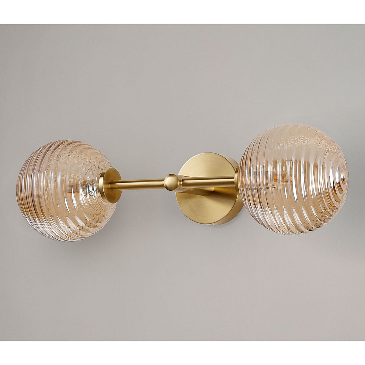 A horizontal brass wall light featuring two amber ribbed glass globes against a grey wall.