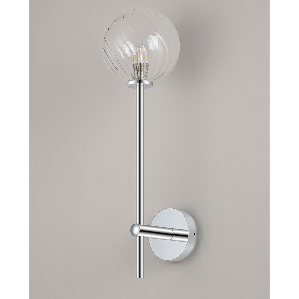 A stylish wall light with a chrome base and a clear, textured glass globe, casting a warm glow.