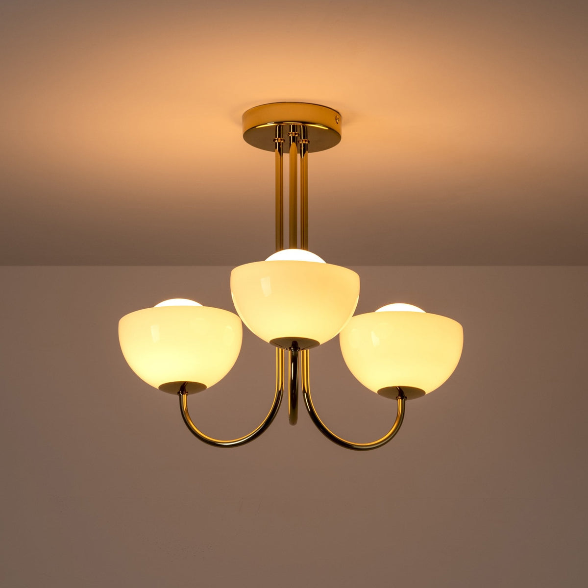 A close up of the lit three-arm chandelier against a white ceiling.