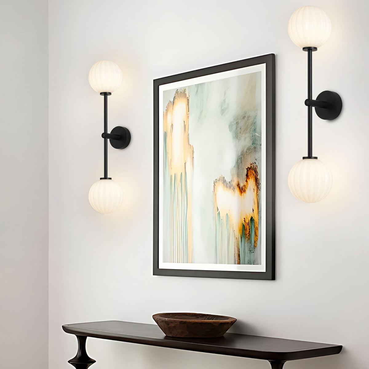 Two black wall lights with white globe shades flanking a piece of abstract art.