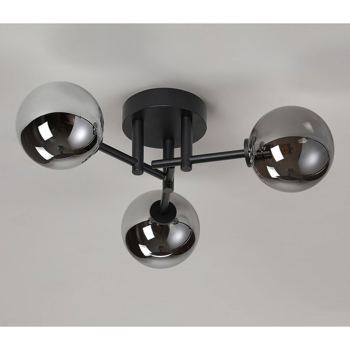 A modern three-sphere ceiling light with smoked glass shades and a black frame, illuminated.