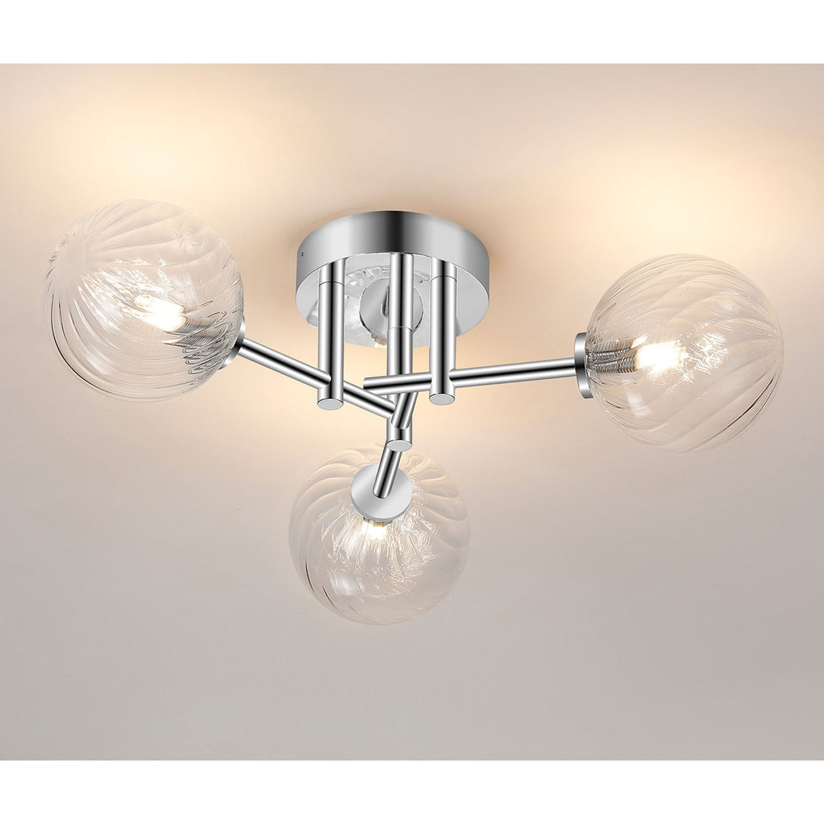 A chrome ceiling light with three clear glass orb shades, illuminated and casting a warm glow.