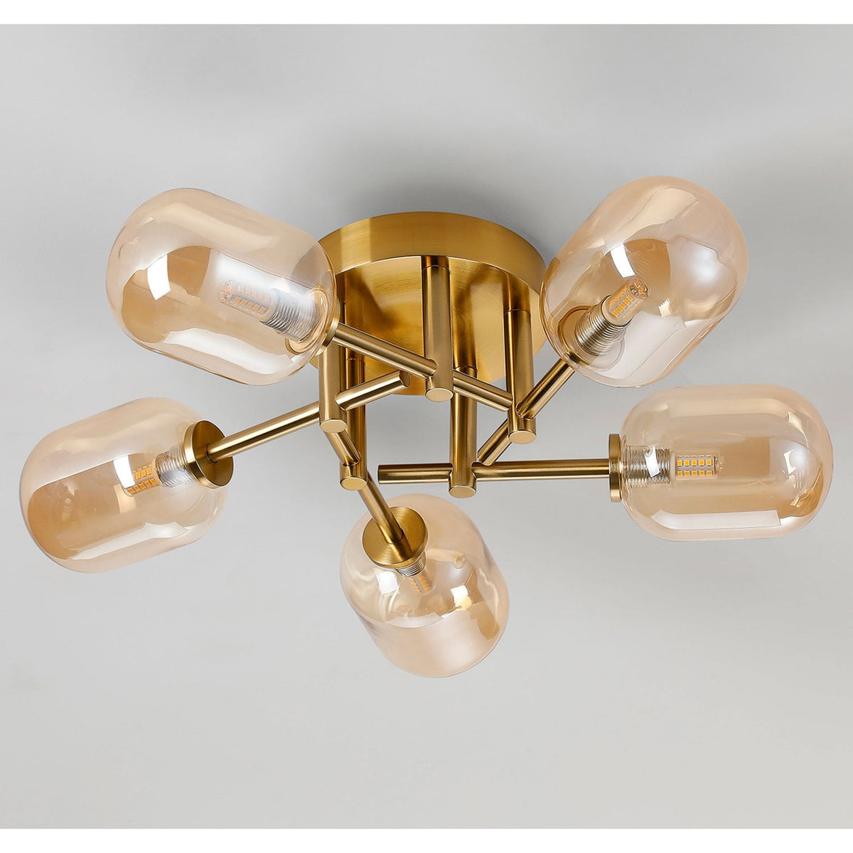 A modern brass ceiling light with five amber glass shades, unlit against a white ceiling.