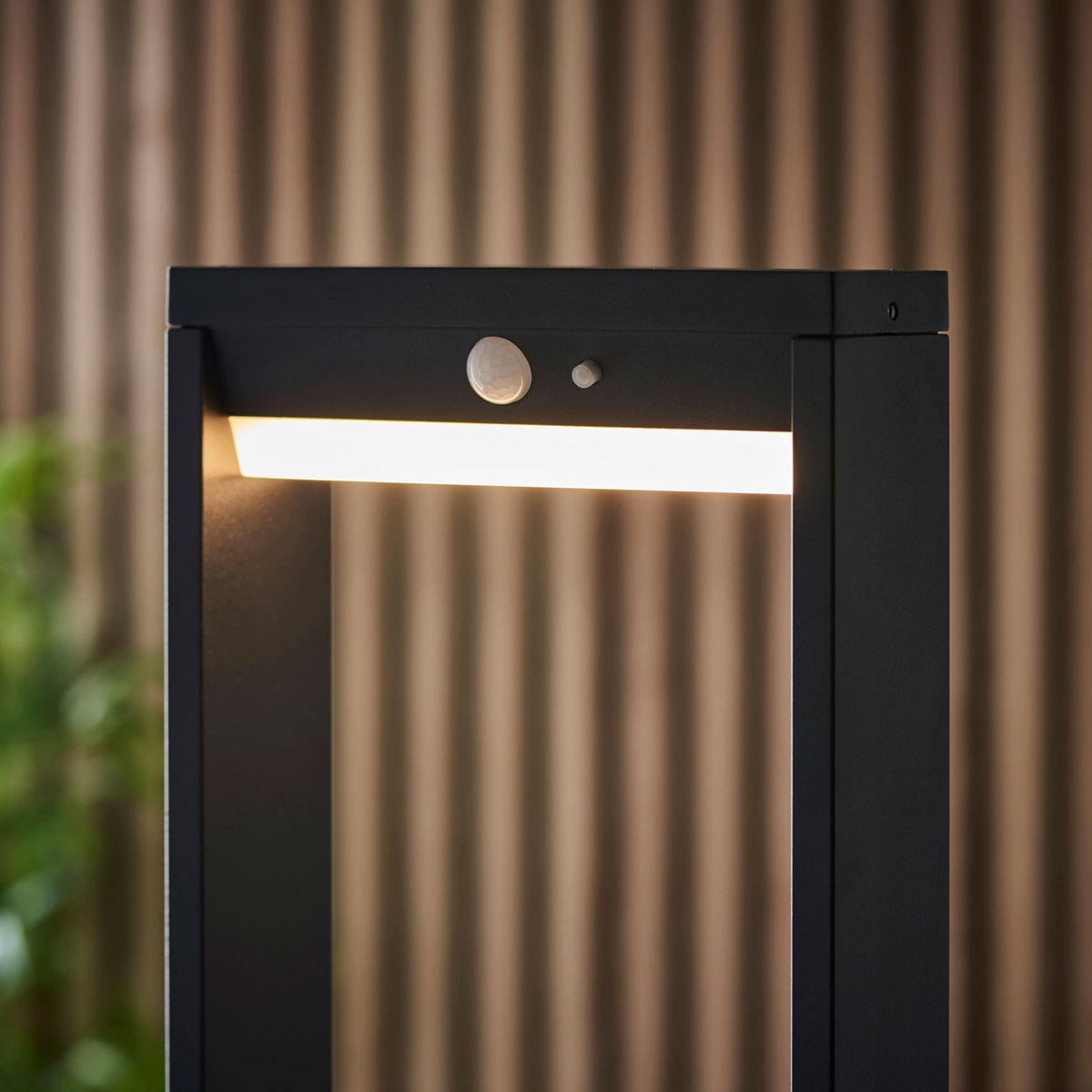 Close-up of the top of a black outdoor bollard light, showing the illuminated strip and motion sensor.