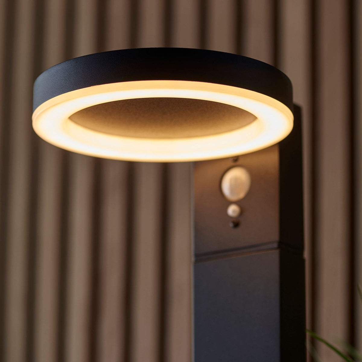 A close-up of the black outdoor light, highlighting its warm circular LED and motion sensor.