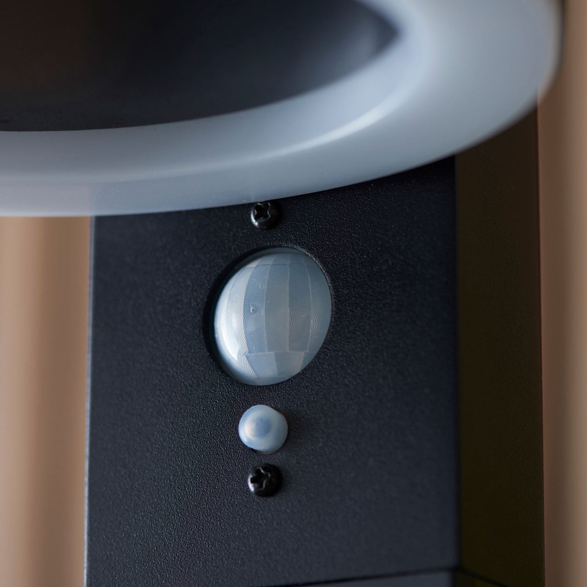 A close-up of the motion sensor on the black outdoor light, with a warm LED glow.