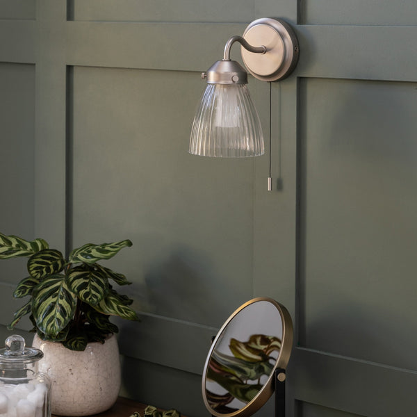 A wall-mounted light fixture with a ribbed glass shade and a pull chain, against a green paneled wall.