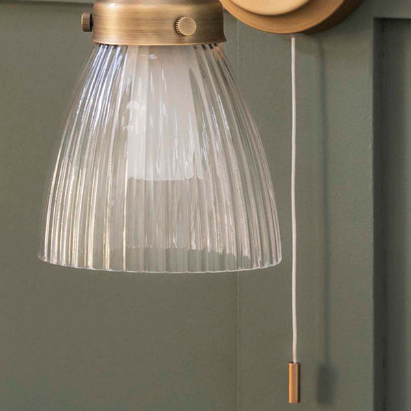 Close-up of a wall light with a fluted glass shade and a brass pull cord.