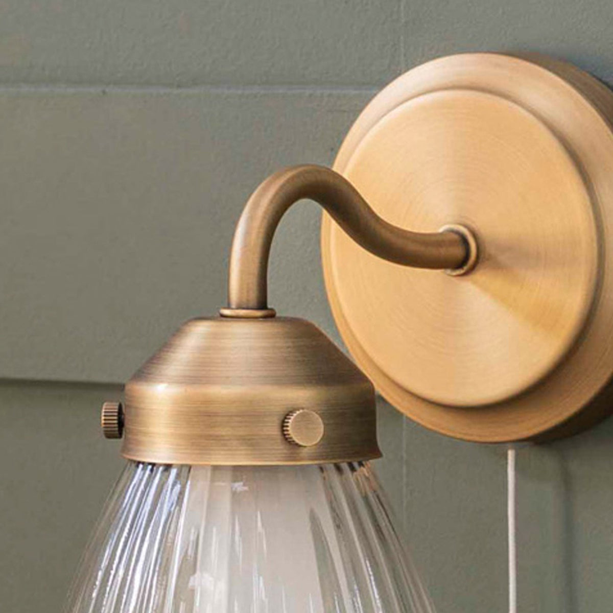 Close-up of a brass wall light with a ribbed glass shade, mounted on a green wall.