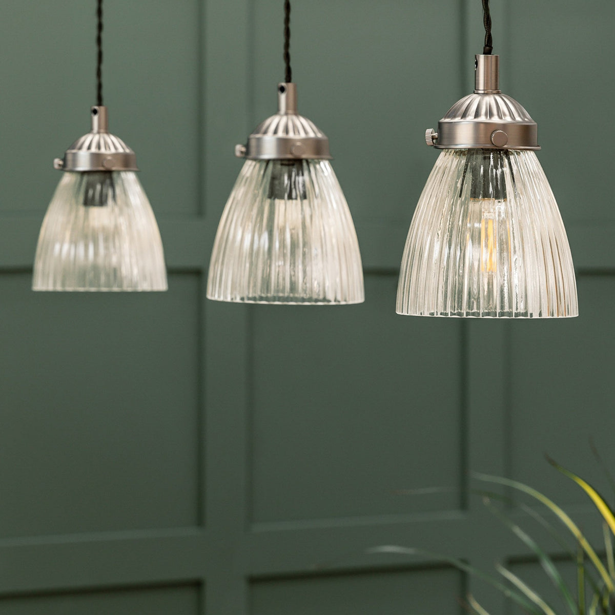Three clear ribbed glass pendant lights with brushed metal fittings hang against a dark green paneled wall.