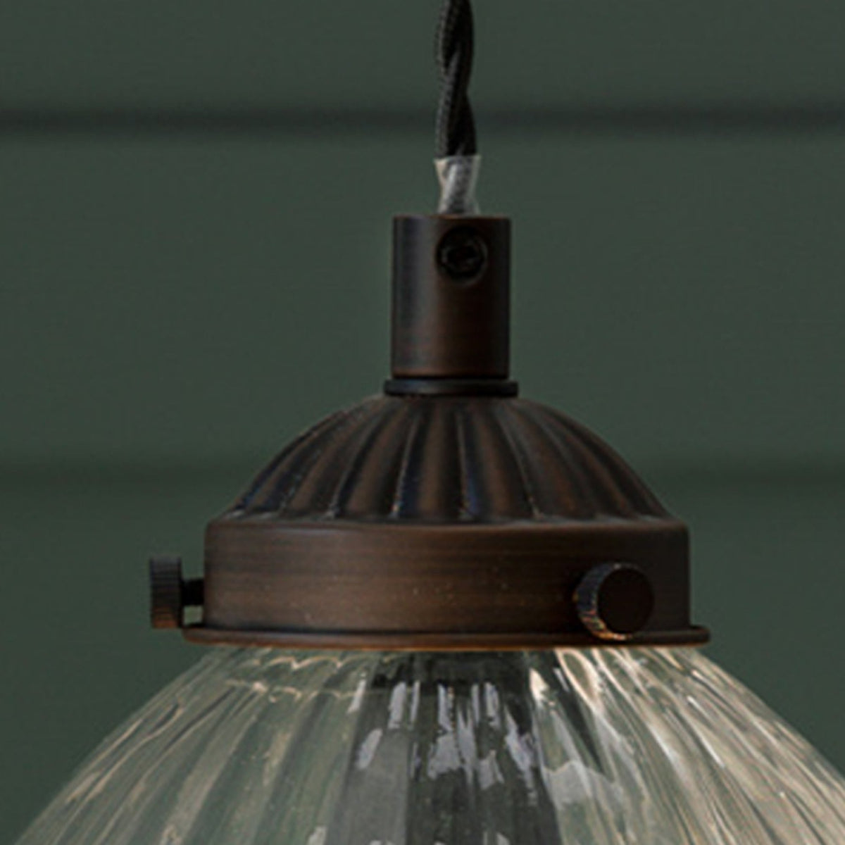 Close-up of a pendant light with a ribbed glass shade and a dark bronze fixture. 