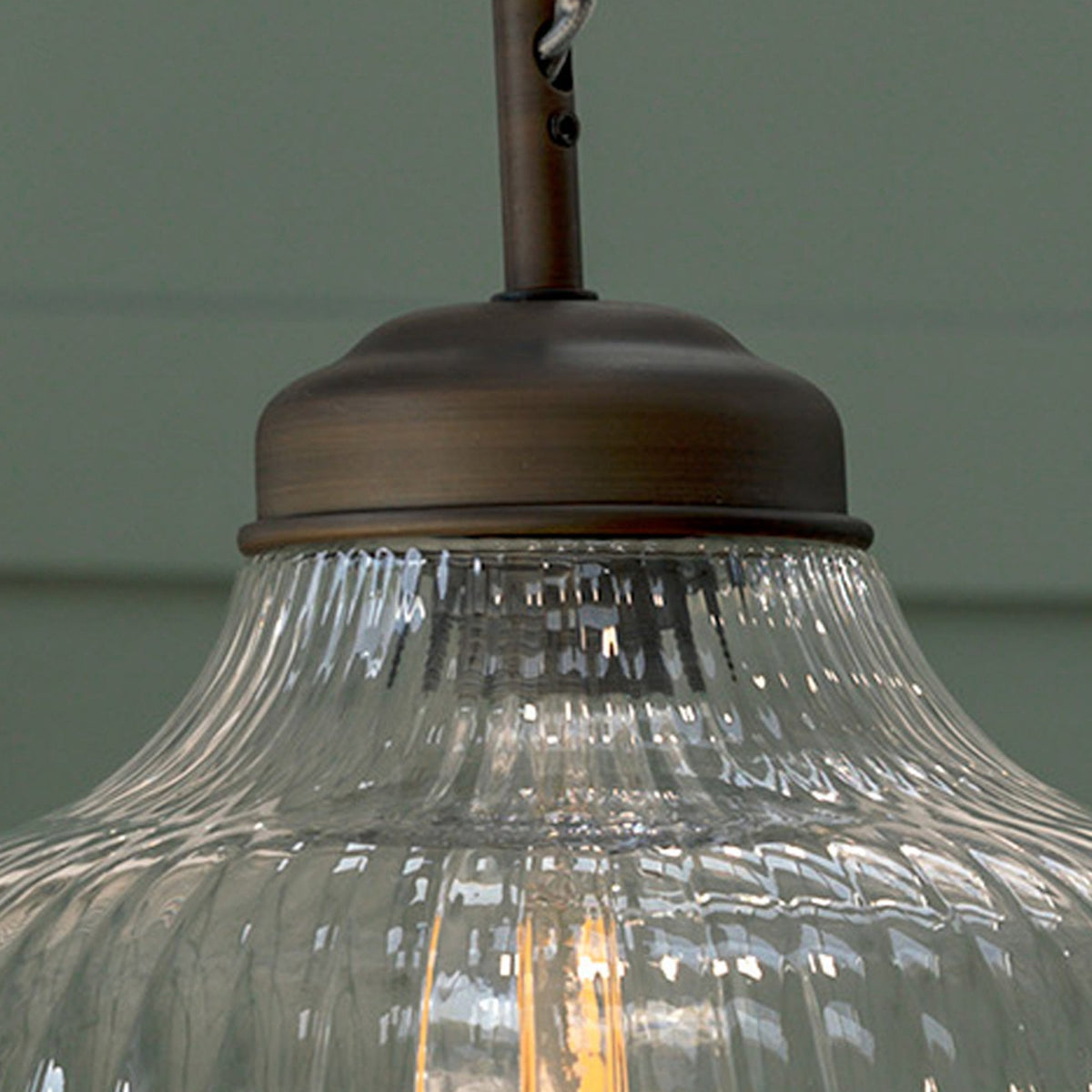 Close-up of a clear, ribbed glass pendant light with a bronze fixture and an illuminated bulb inside. 