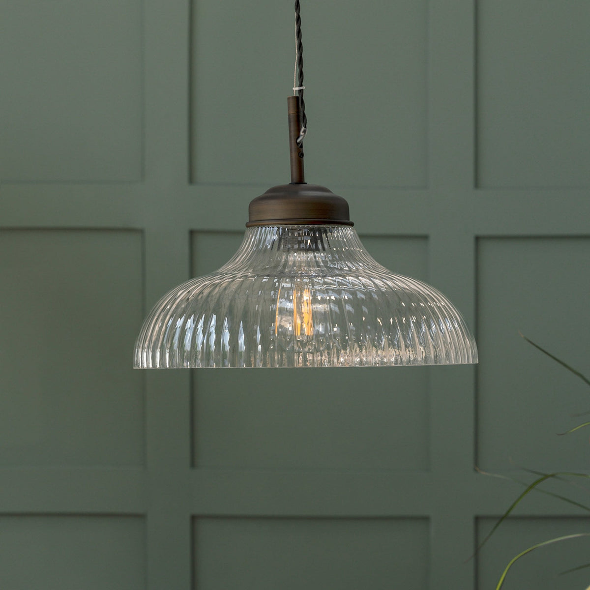 Ribbed glass pendant light with a bronze fitting, illuminating a dark green paneled wall.