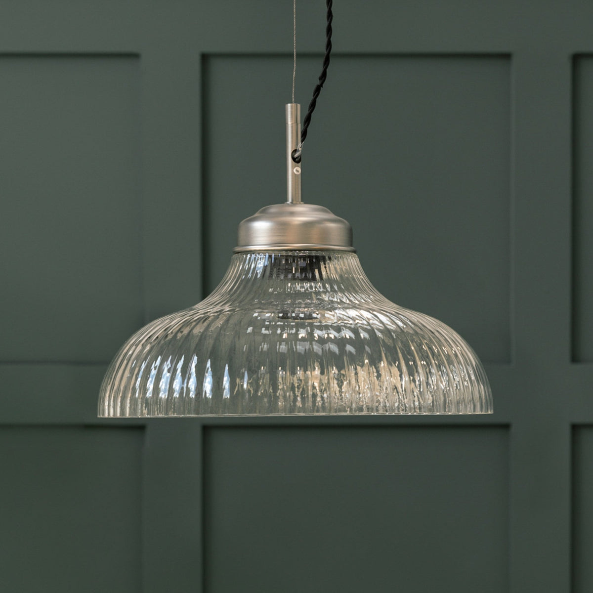 Ribbed glass pendant light with a brushed steel fitting against a dark green paneled wall. 