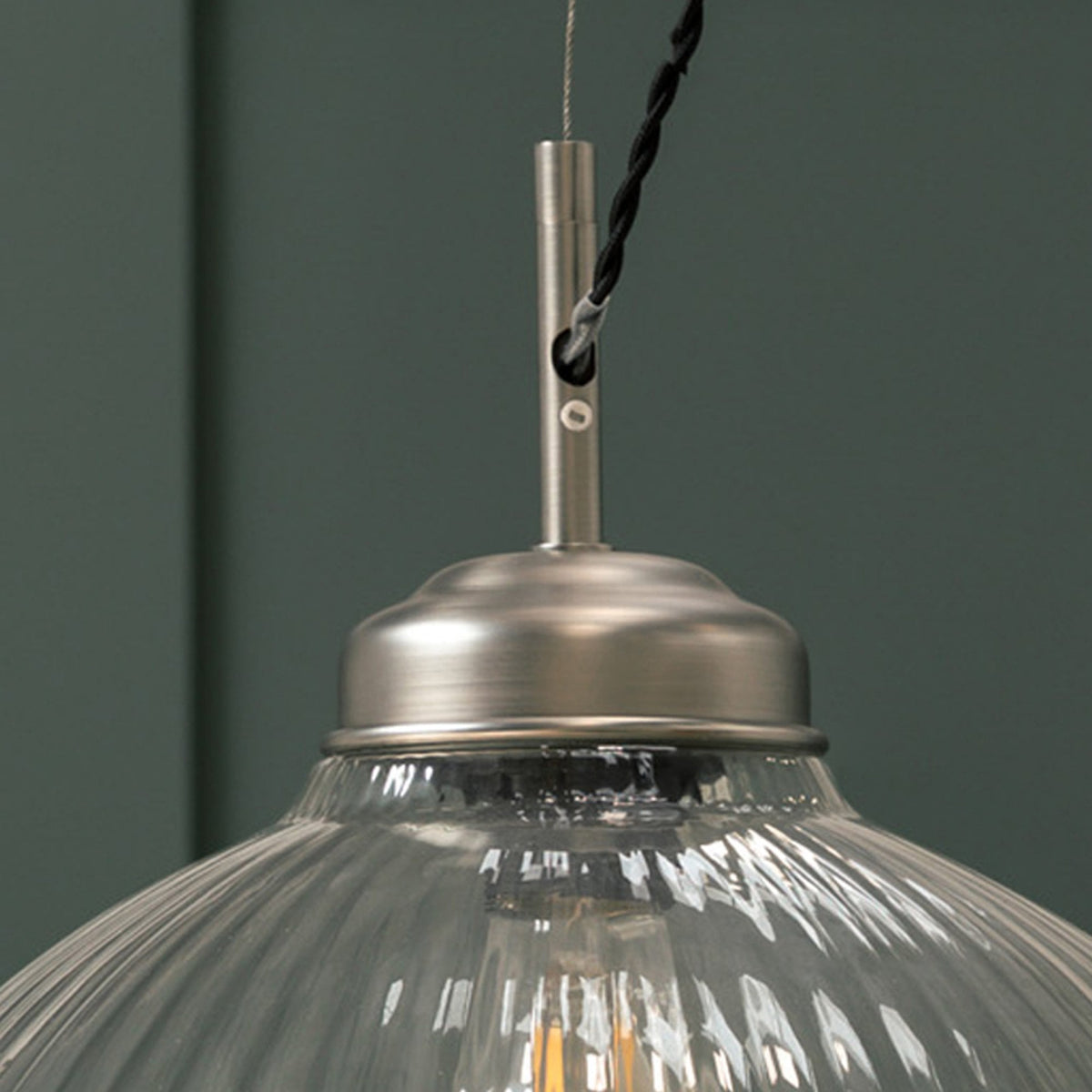 Close-up of a ribbed glass pendant light with a brushed metal fitting and black braided cord.