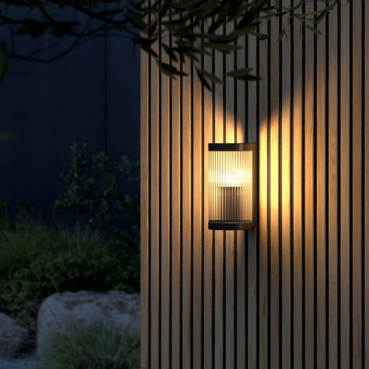 An outdoor wall light with a black frame and reeded glass casts a warm glow on a wooden wall.
