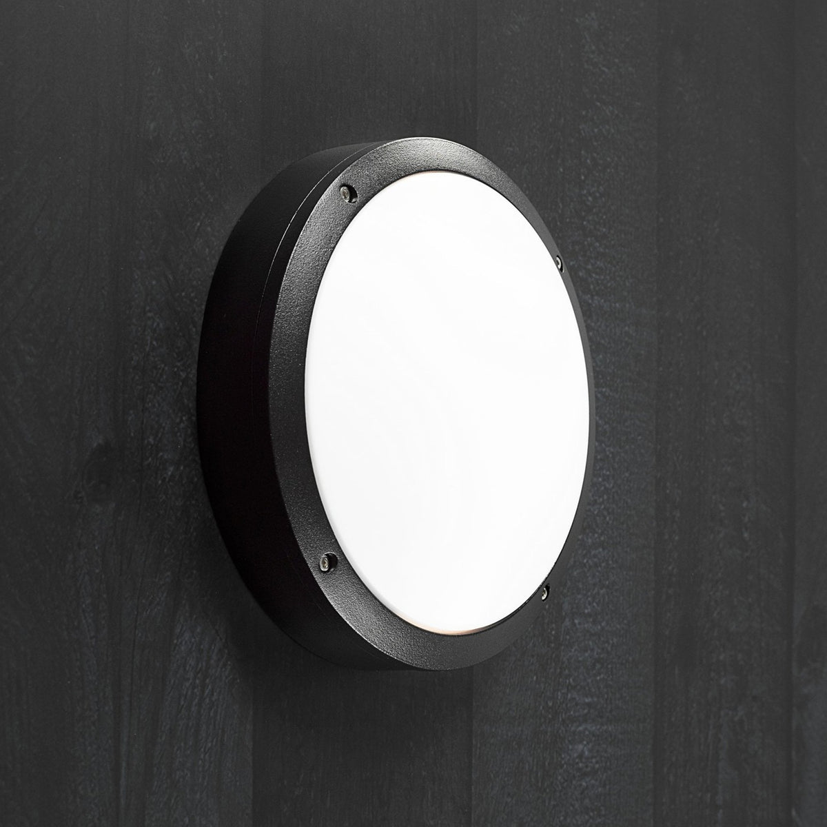 A round black ceiling or wall light with a white diffuser, mounted on a dark wooden surface.