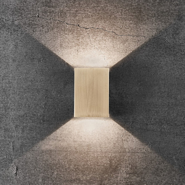 A golden rectangular wall light illuminates a textured grey wall with light directed both upwards and downwards.