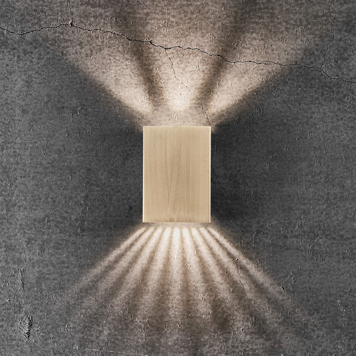 A golden rectangular wall light illuminating a textured grey wall, with intricate light patterns.
