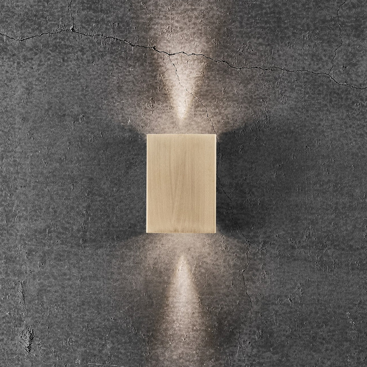 A golden rectangular wall light illuminates a textured grey wall with narrow beams of light.