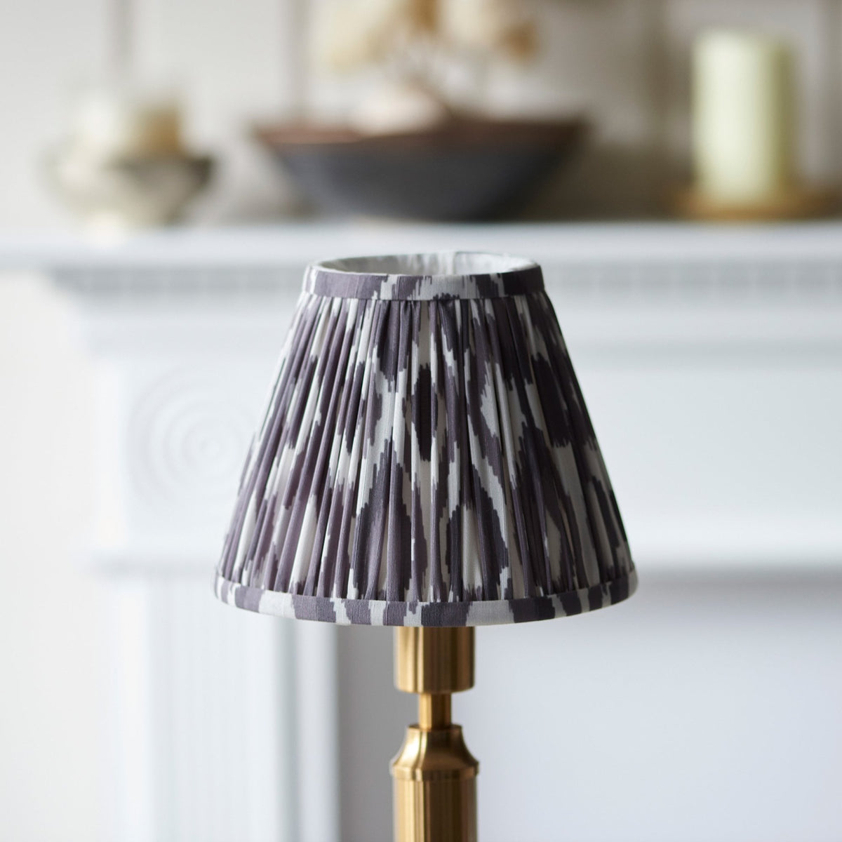 Close-up of a pleated ikat lampshade on a gold lamp base in a dining room setting.