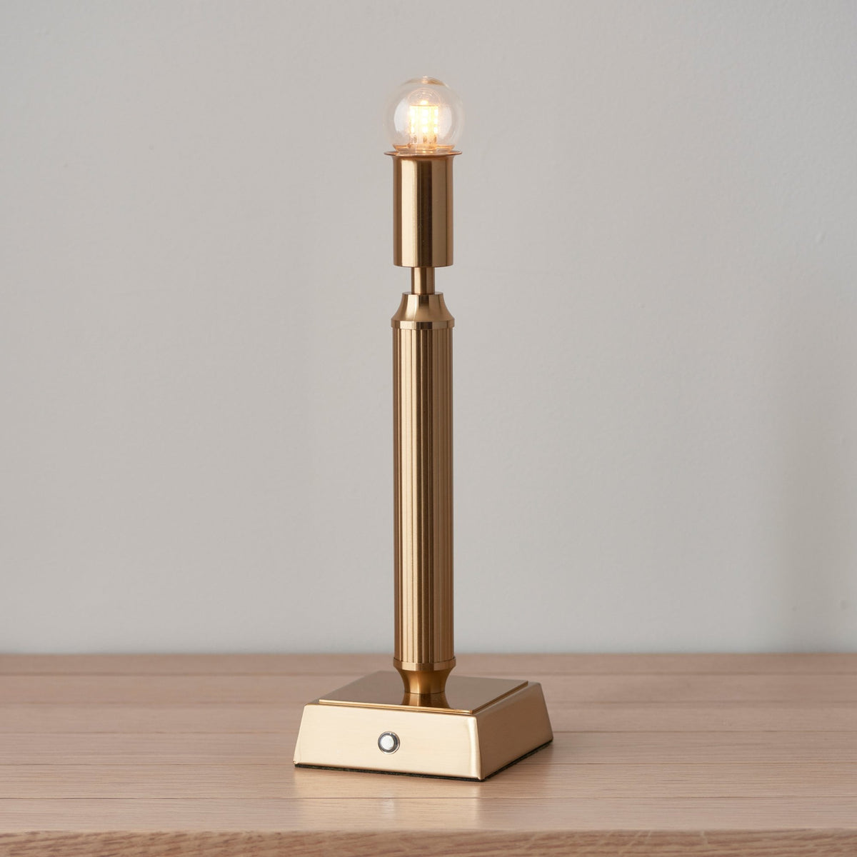 A gold-coloured rechargeable table lamp without a shade, showing the light bulb.