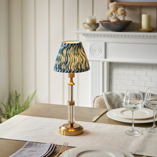 A small table lamp with a patterned shade sits on a dining table with place settings.