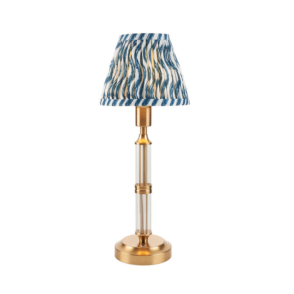 A small table lamp with a clear and brass base and a blue patterned shade on white.