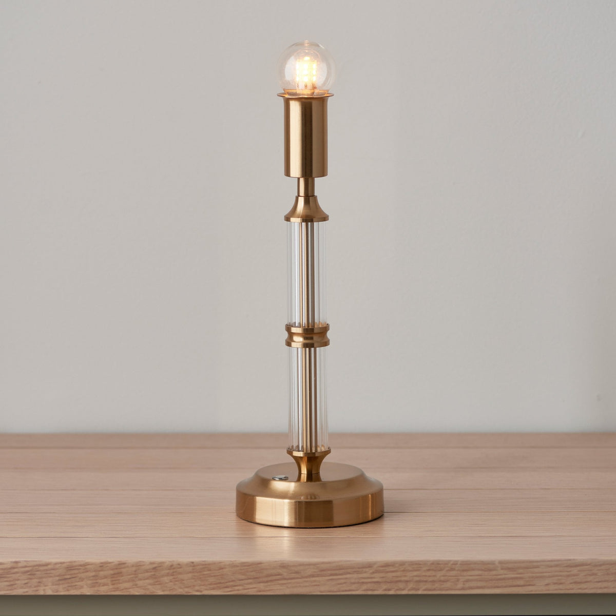 A table lamp base with a brass and clear glass stem and exposed bulb.
