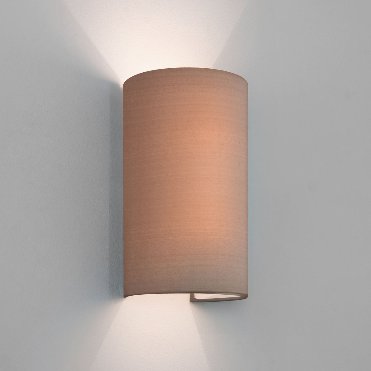 Cylindrical wall light with a beige fabric shade, casting light upwards and downwards on a white wall
