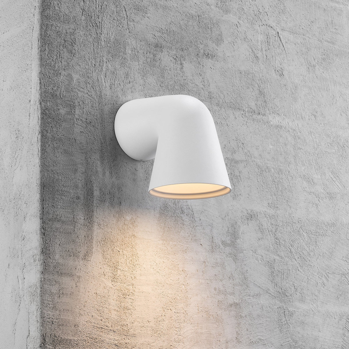 White wall-mounted light fixture illuminating a grey concrete wall.