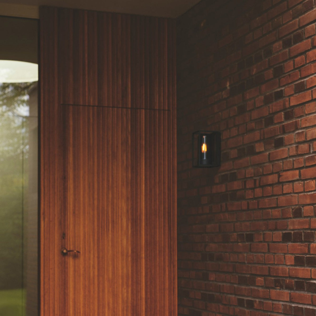 A black outdoor wall light with a glowing filament bulb on a brick wall.