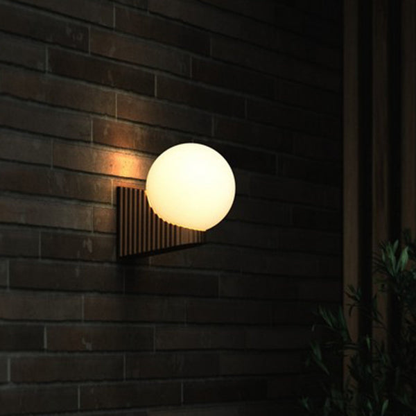 A round wall light with a striped dark brown base casting warm light on a brick wall.