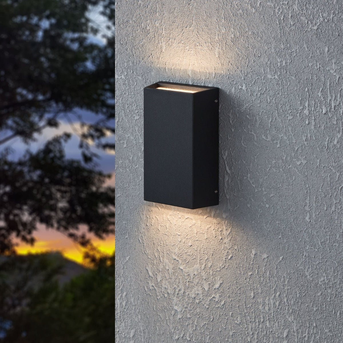 A black outdoor wall light illuminates an exterior wall at dusk.