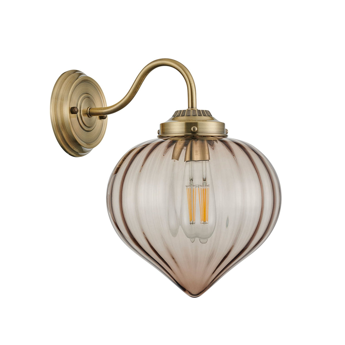 A brass wall light with a clear, fluted glass shade housing an unlit filament bulb.
