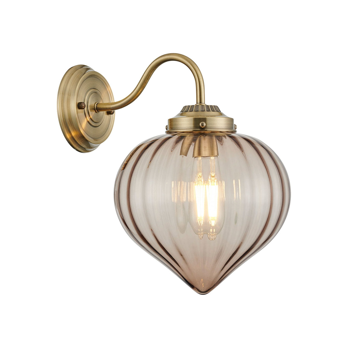 A brass wall light with a clear, fluted glass shade housing a lit filament bulb.