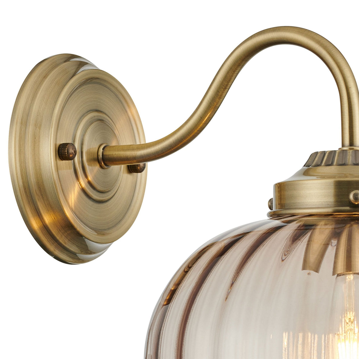 Close-up of the brass wall mount and curved arm of the wall light with a clear shade.