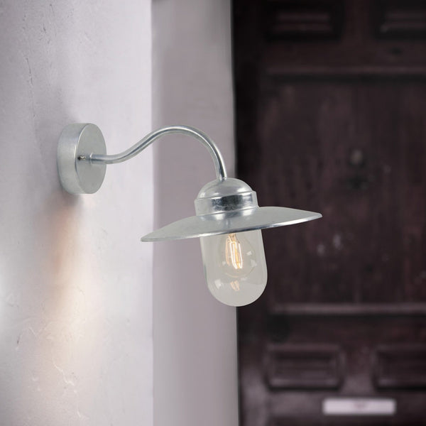 Silver outdoor wall light with a curved arm, a wide brim, and a clear glass bulb casing.