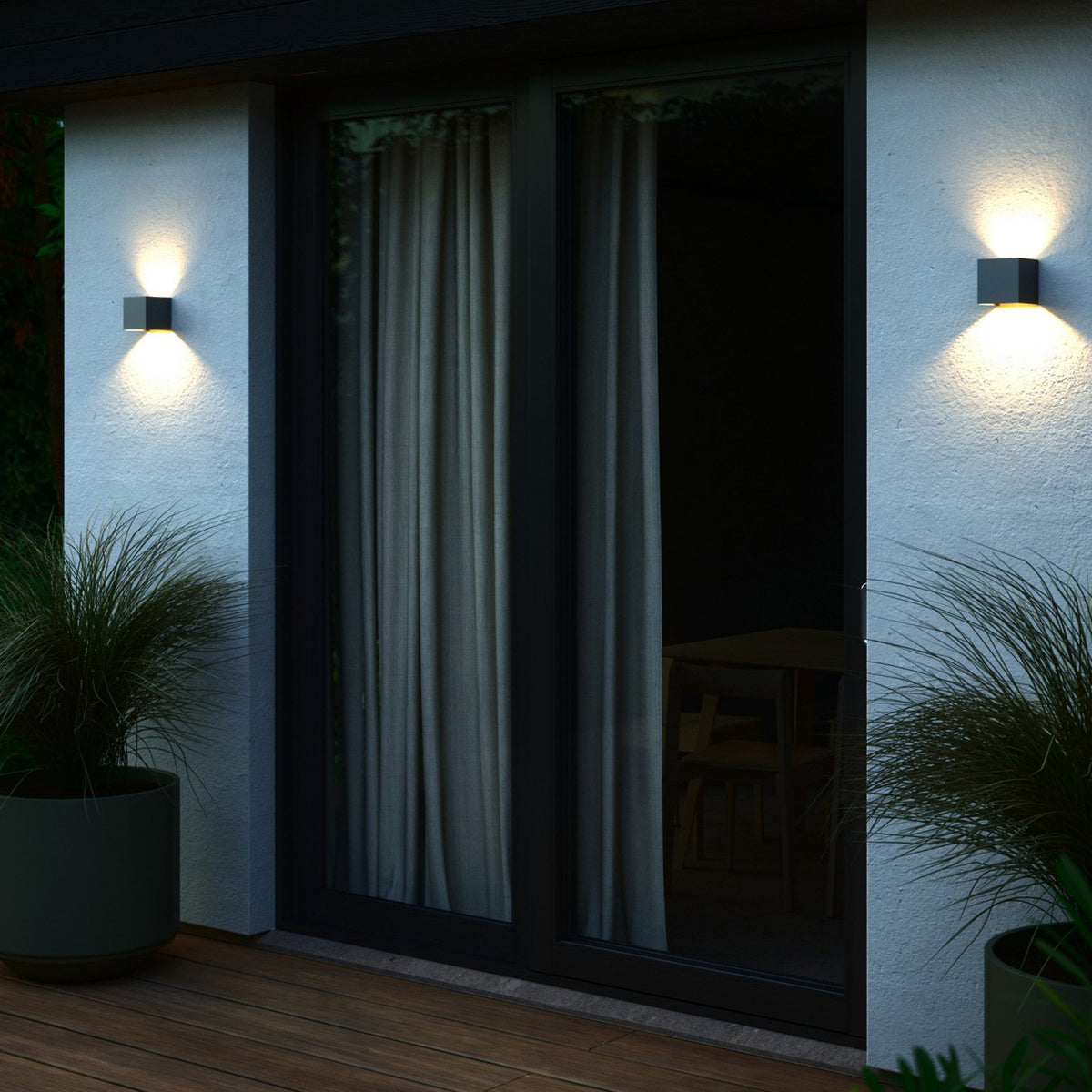 Two anthracite cube wall lights illuminate a modern patio at dusk.
