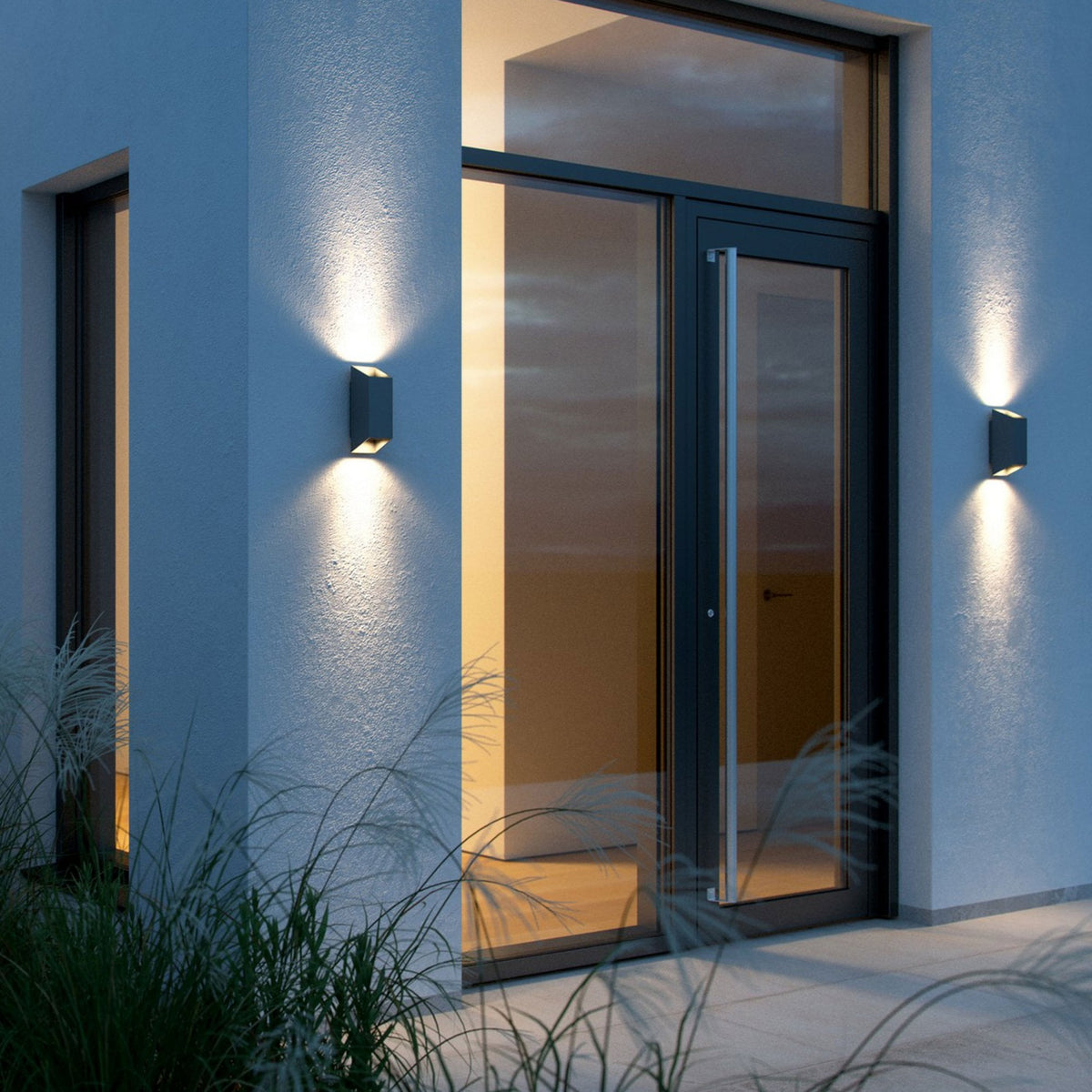 Two modern outdoor lights on a white wall illuminating the space below.