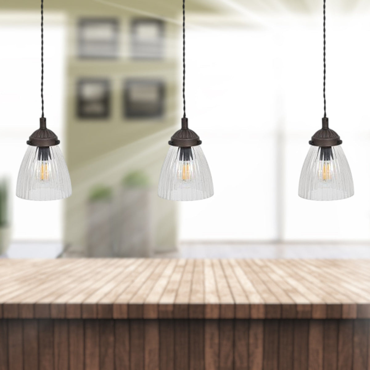 Three pendant lights with clear ribbed glass shades hang over a wooden counter.