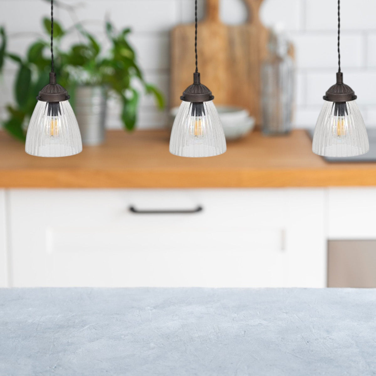 Three pendant lights with ribbed glass shades hang over a kitchen counter.