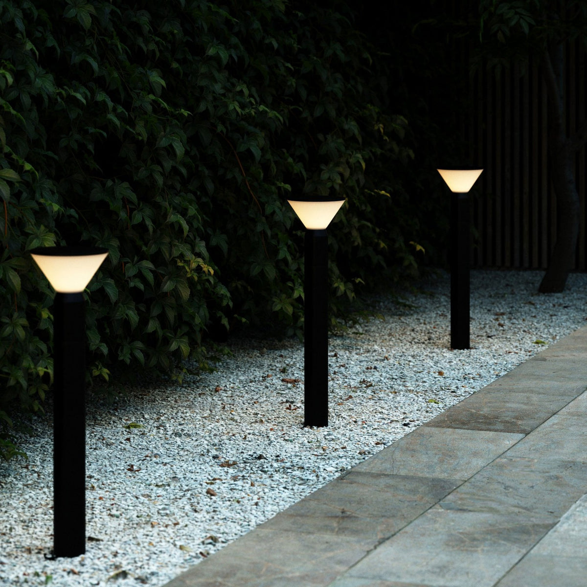 Three illuminated bollard lights lining a garden path at night, providing ambient lighting.