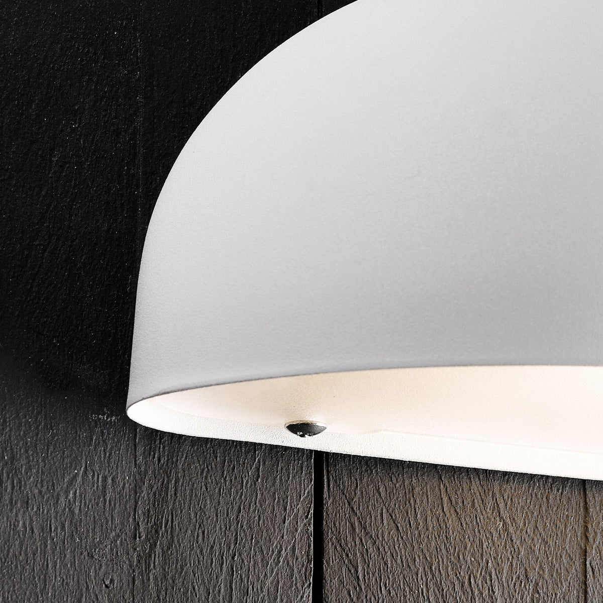 A close-up of the underside of the half-dome outdoor wall light against a dark wooden wall.