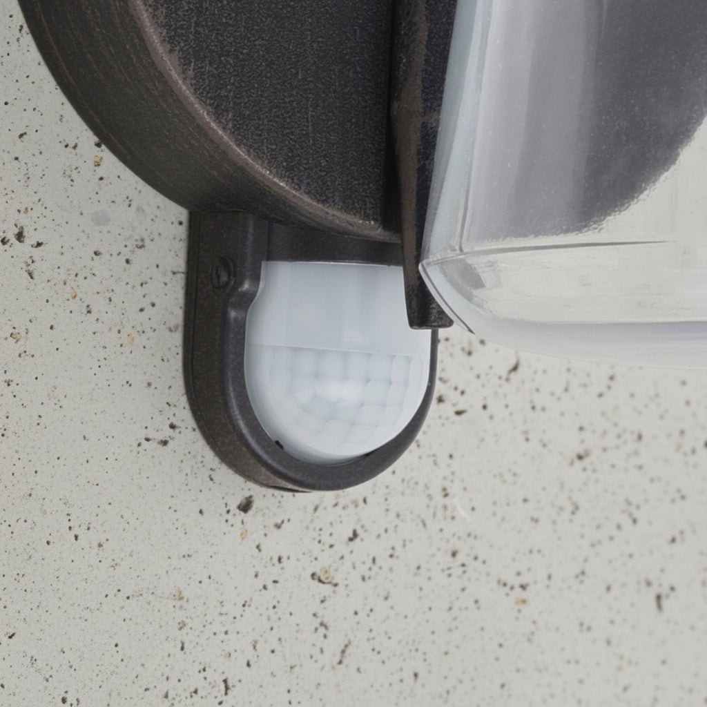 Close-up of a motion sensor on an outdoor light fixture, mounted on a textured wall.