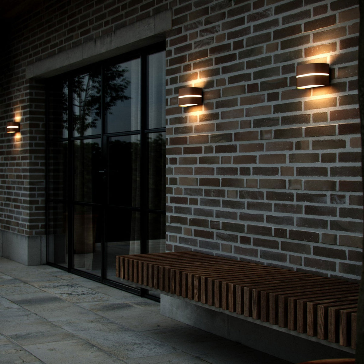 Three oval-shaped, dark grey outdoor wall lights with a horizontal glow illuminate a brick wall.