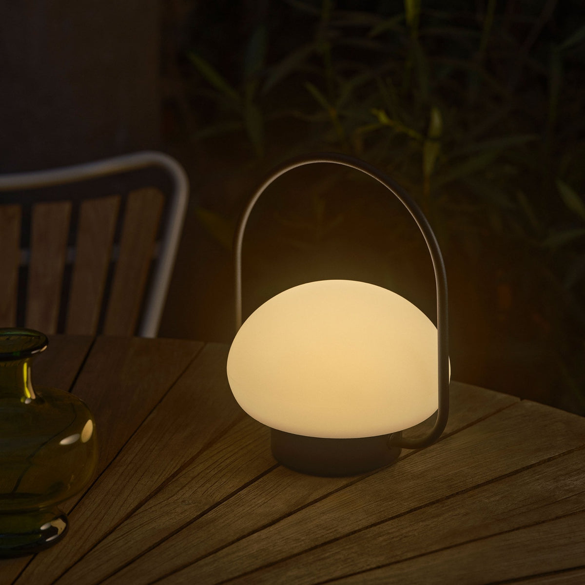 A portable outdoor mushroom lamp sits on a wooden table at night, emitting a warm glow.