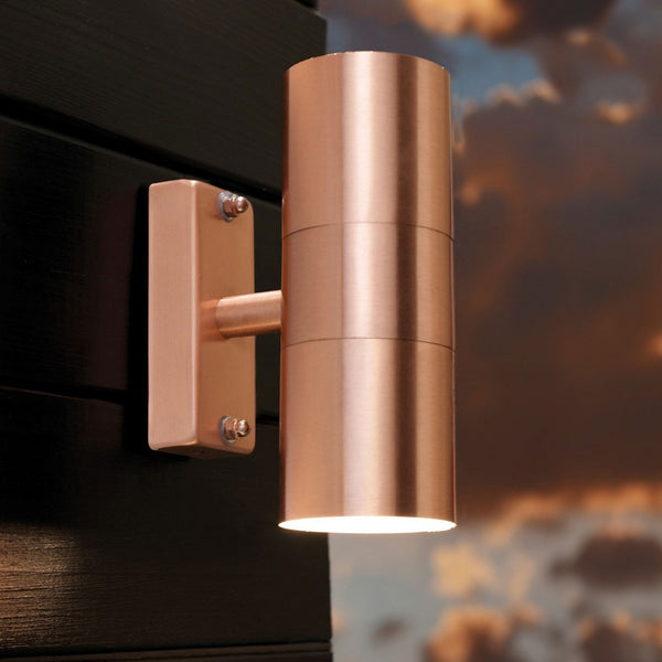 An outdoor copper up-and-down wall light illuminates a dark wall at dusk.